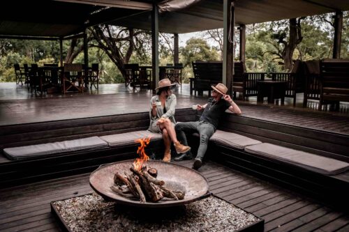 Couple relaxing by the firepit at Honeyguide Khoka Moya Camp’s outdoor lounge area